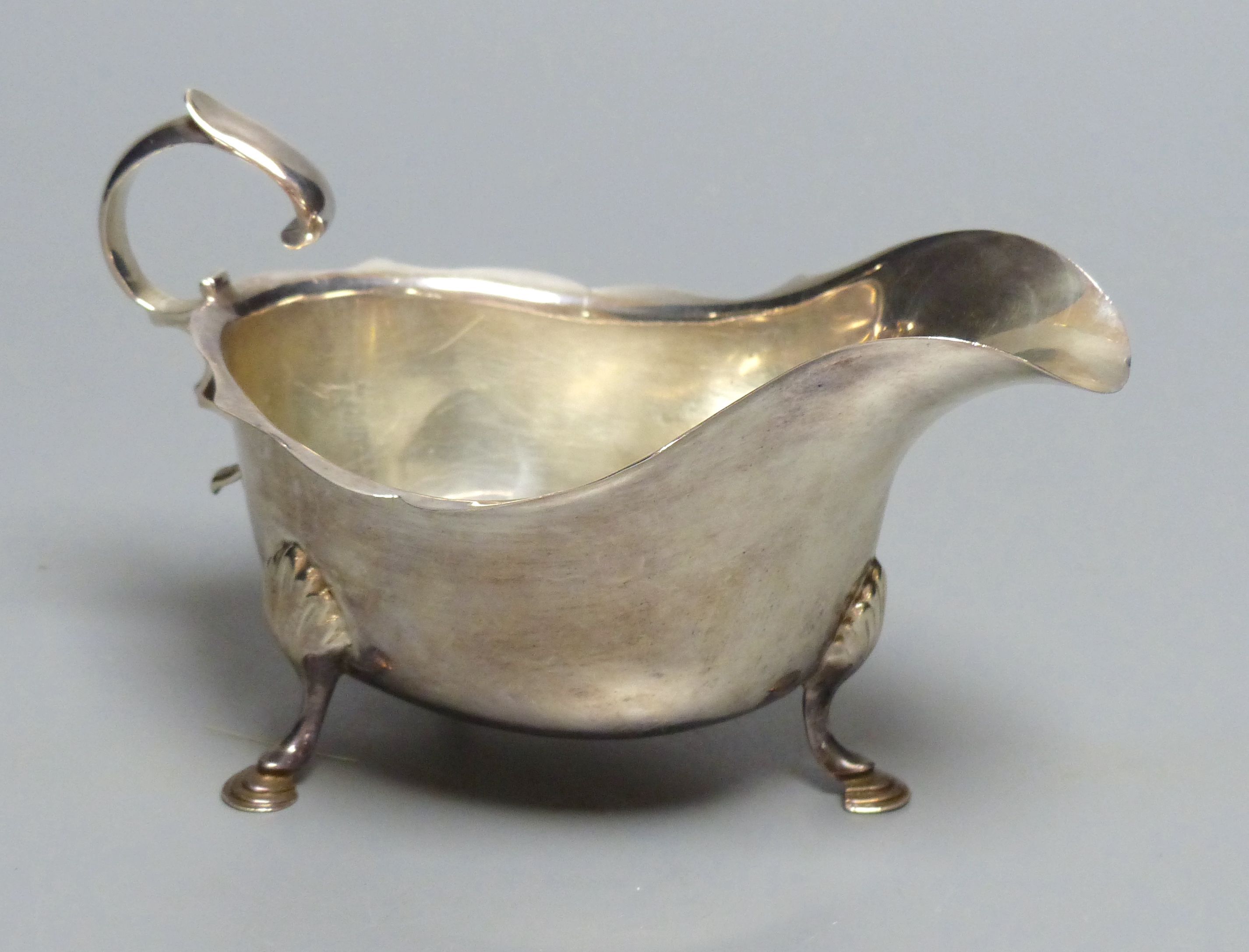 A silver sauce boat, having shaped edge, flying scroll handle and three hoof feet, marks rubbed, 4oz.